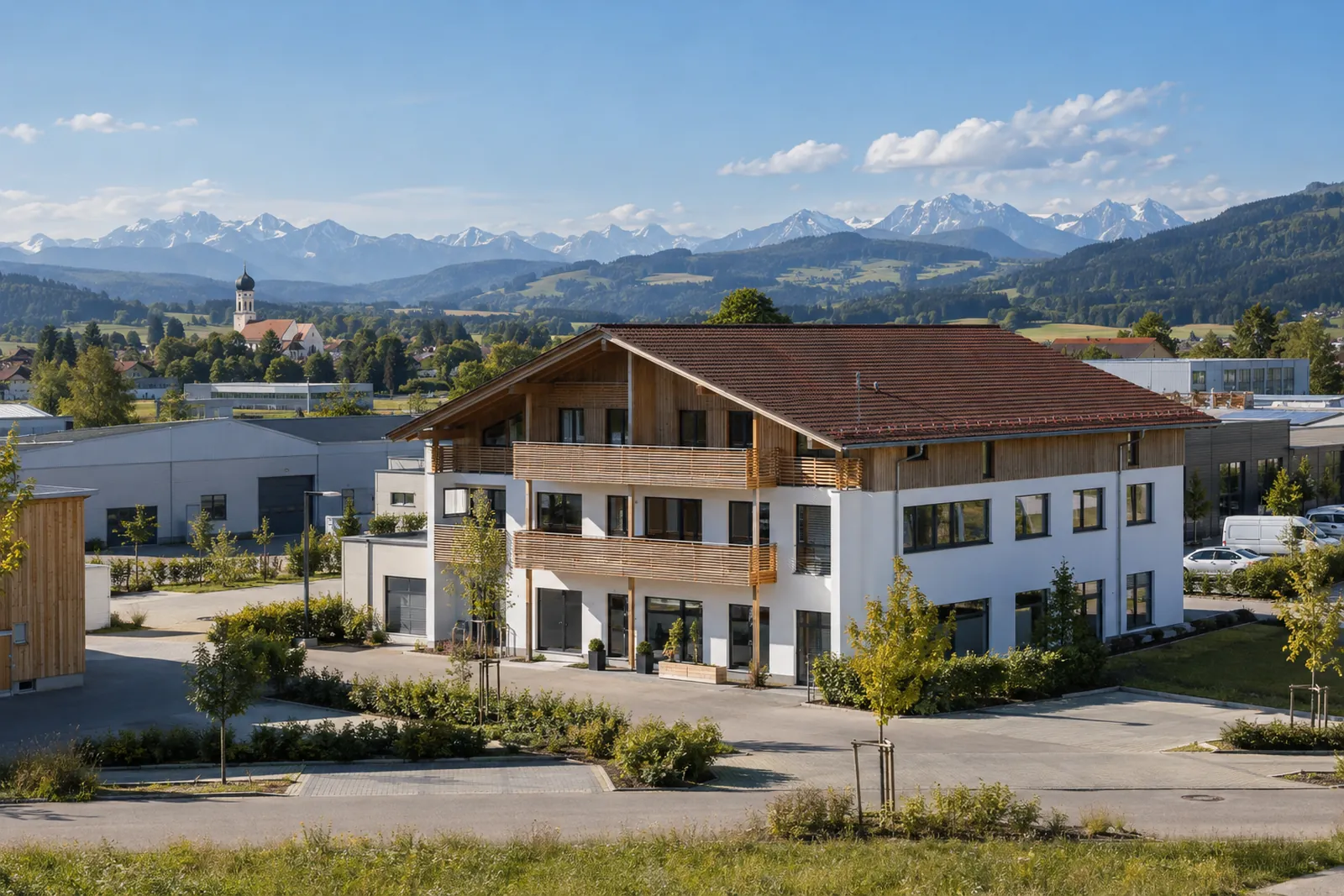 Gewerbebau mit Satteldach in einem oberbayerischen Gewerbegebiet, im Hintergrund Voralpenland und Alpenkette