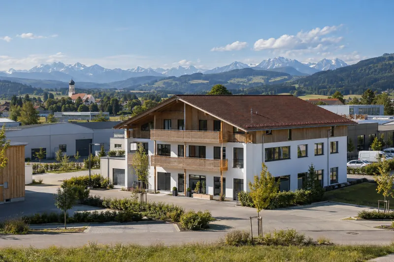 Gewerbebau mit Satteldach in einem oberbayerischen Gewerbegebiet, im Hintergrund Voralpenland und Alpenkette