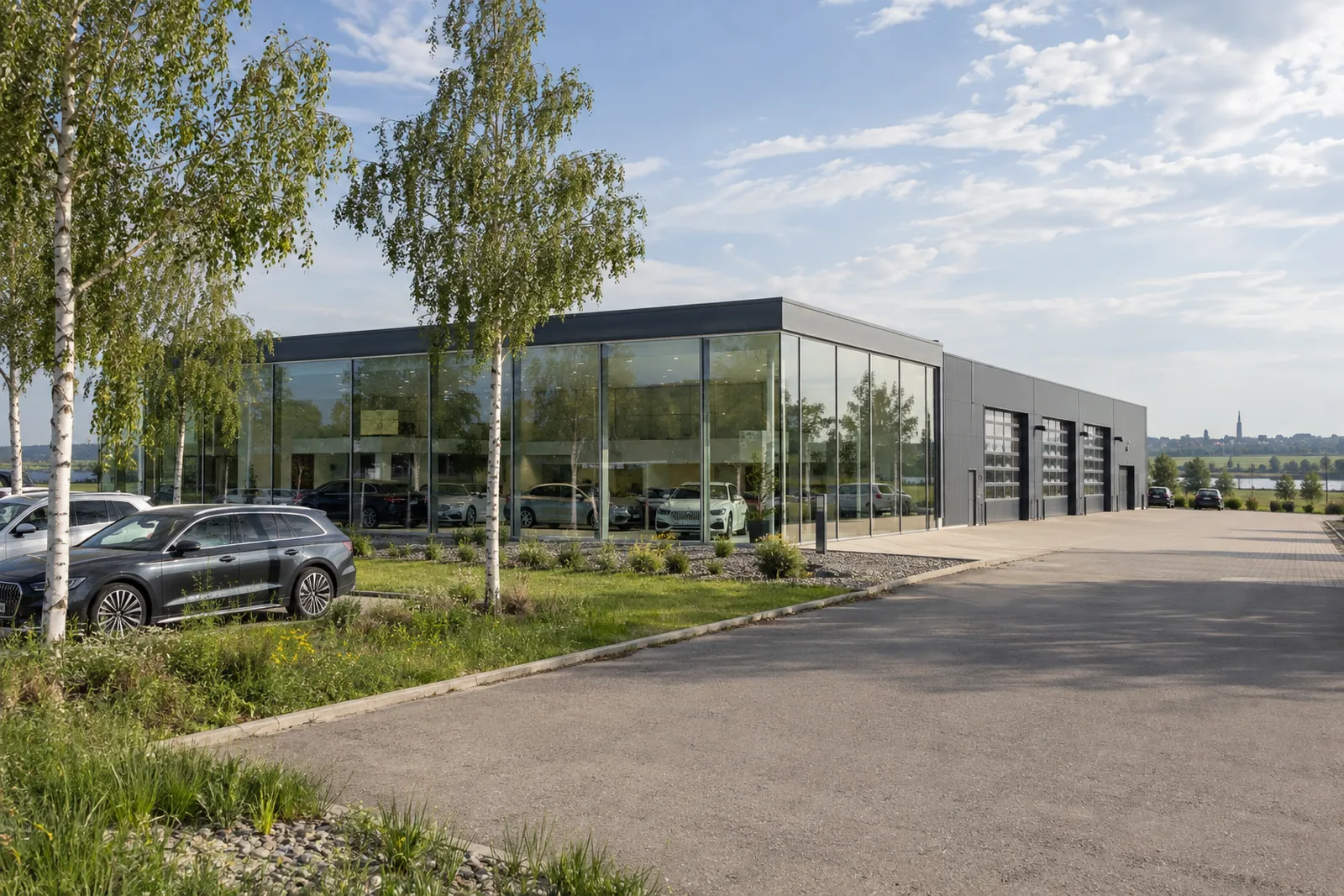 Autohaus mit gläsernem Showroom und angebauter Werkstatthalle am Stadtrand, davor geparkte Fahrzeuge