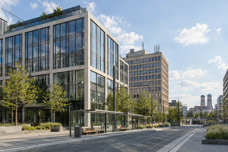 Moderner Bürobau neben einem Bürohaus der 1970er Jahre in München, im Hintergrund die Türme der Frauenkirche