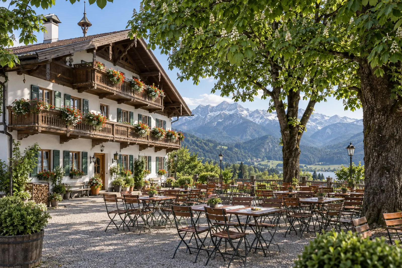 Oberbayerischer Gasthof mit Holzbalkon und leerem Biergarten vor Alpenkulisse