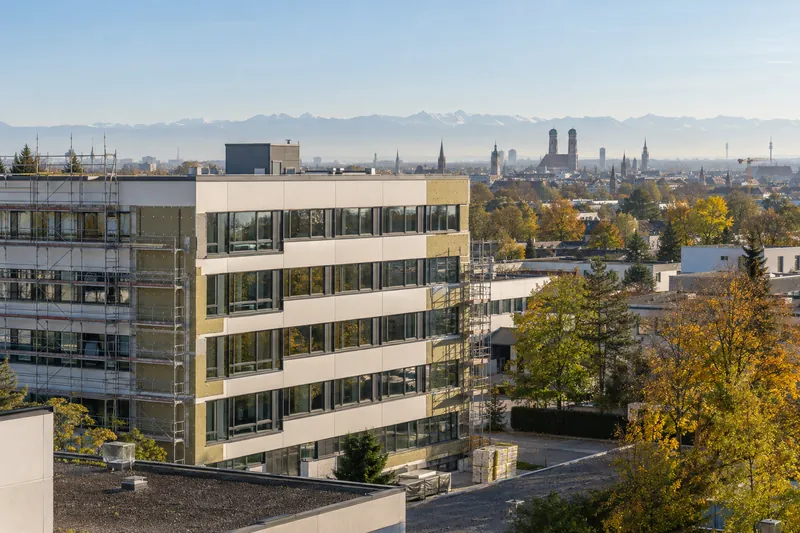 Sanierter Bürobau der Nachkriegszeit am Münchner Stadtrand mit neuer Fassade, im Hintergrund die Türme der Frauenkirche
