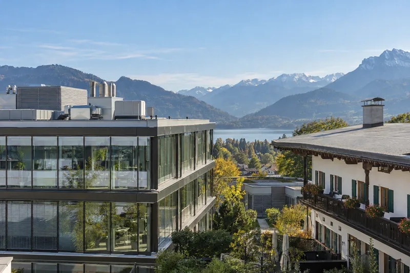 Bürogebäude mit Lüftungsgeräten auf dem Dach neben einem oberbayerischen Gasthof, im Hintergrund Alpenvorland