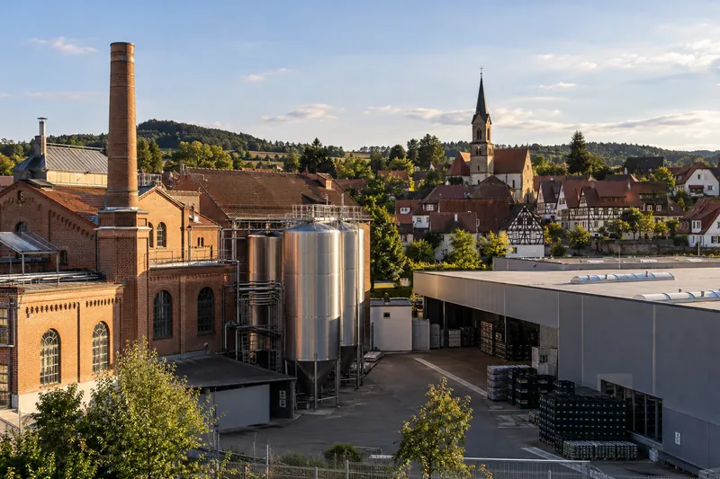 Backsteinbrauerei und moderne Lagerhalle in einer fränkischen Kleinstadt mit Fachwerkhäusern im Hintergrund