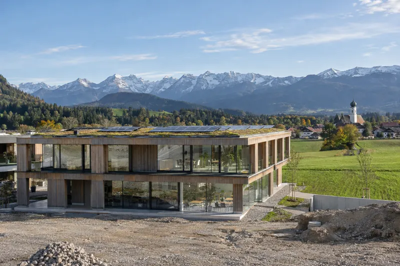 Neu gebautes Gewerbegebäude mit Holz-Glas-Fassade und Solardach vor Alpenpanorama in Oberbayern