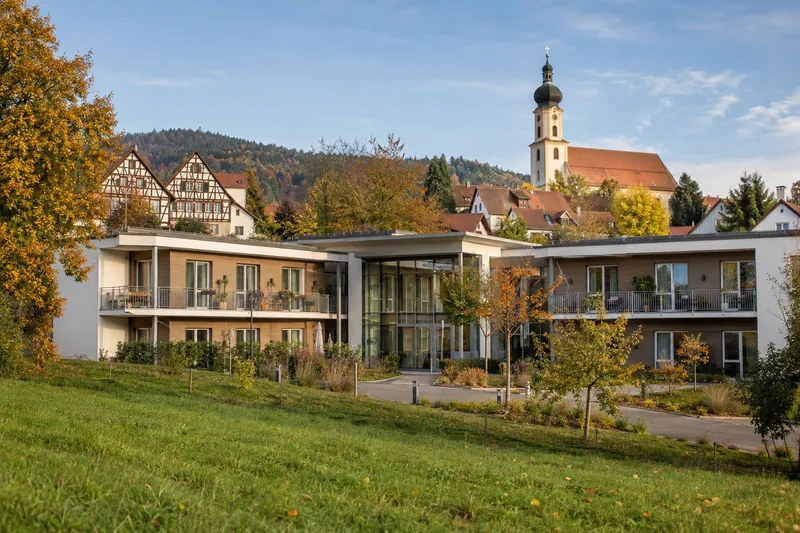 Zweigeschossiges Pflegeheim mit Balkonen in einer bayerischen Kleinstadt, dahinter Fachwerkhäuser und ein Kirchturm