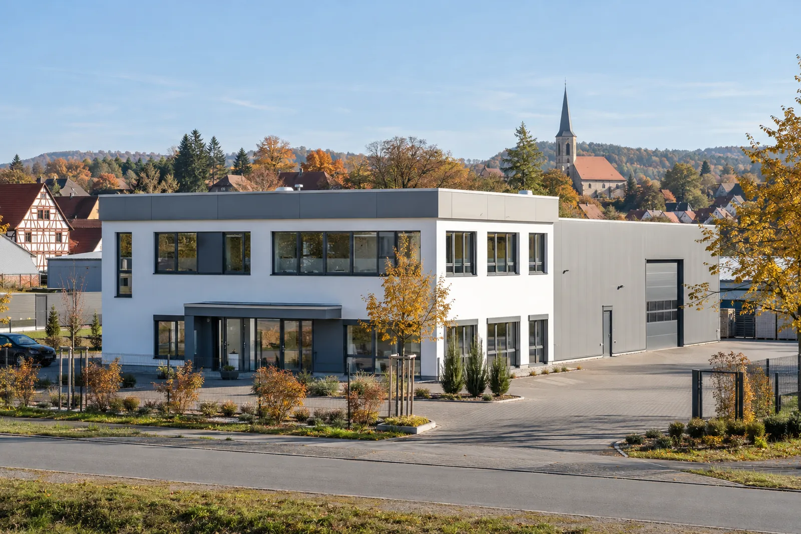 Gewerbebau mit Werkstatthalle in einem mittelfränkischen Gewerbegebiet, im Hintergrund Fachwerkhäuser und ein Kirchturm