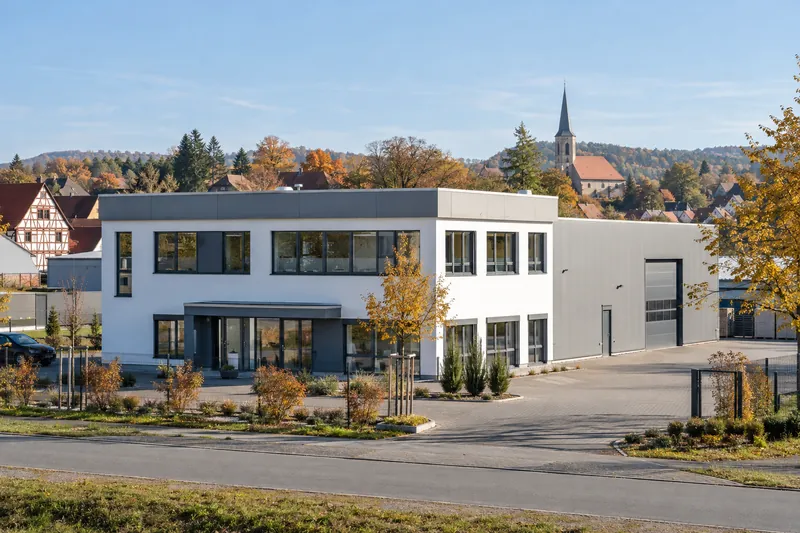 Gewerbebau mit Werkstatthalle in einem mittelfränkischen Gewerbegebiet, im Hintergrund Fachwerkhäuser und ein Kirchturm