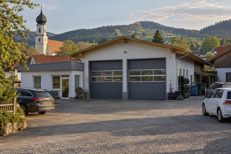 Kfz-Werkstatt mit zwei Sektionaltoren und Büroanbau in einem niederbayerischen Dorf, im Hintergrund ein Zwiebelturm und Hügel