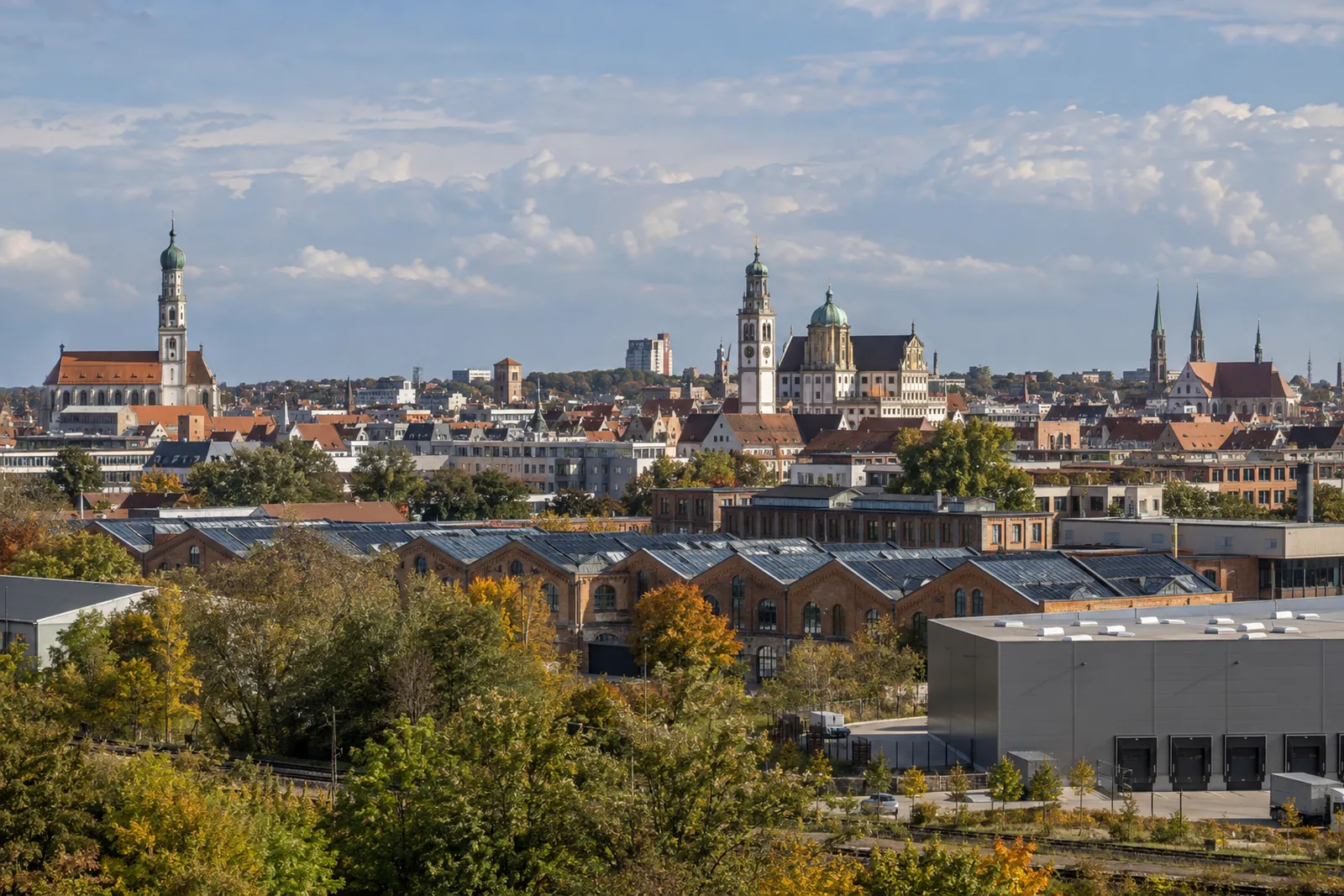 Augsburger Stadtsilhouette mit Türmen, umgenutzten Backsteinfabriken im Textilviertel und moderner Halle