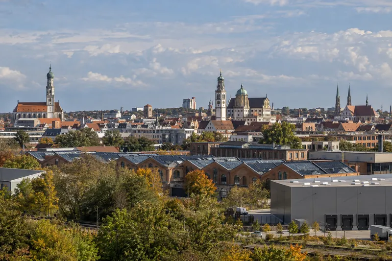 Augsburger Stadtsilhouette mit Türmen, umgenutzten Backsteinfabriken im Textilviertel und moderner Halle