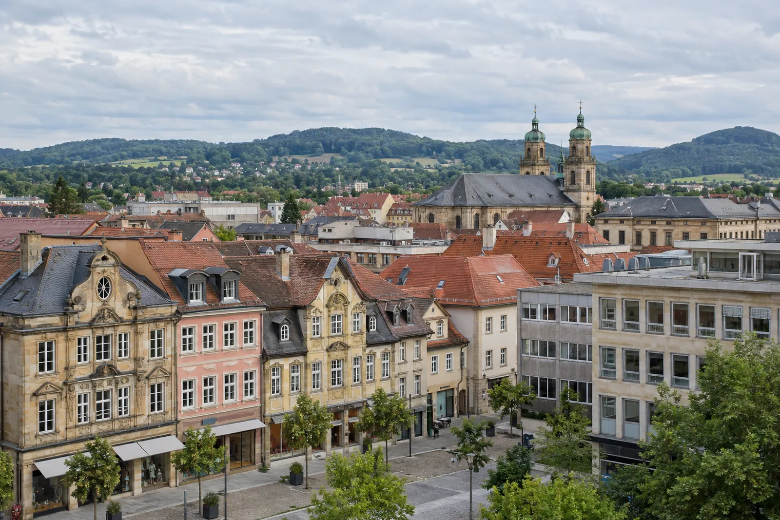 Geschäftshäuser in der Bayreuther Innenstadt, barocke Fassaden neben Nachkriegsbauten, im Hintergrund grüne Hügel