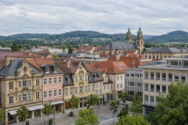 Geschäftshäuser in der Bayreuther Innenstadt, barocke Fassaden neben Nachkriegsbauten, im Hintergrund grüne Hügel