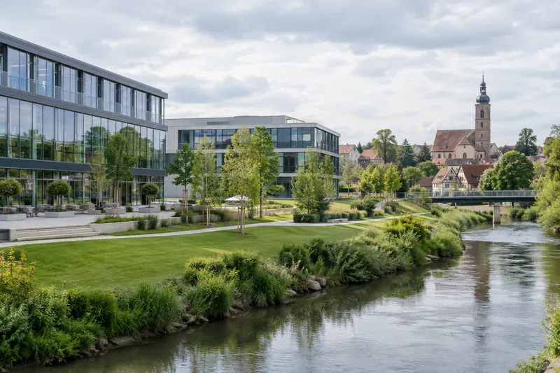 Moderner Bürokomplex mit Glasfassade und Rasenfläche, dahinter Altstadt mit Kirchturm