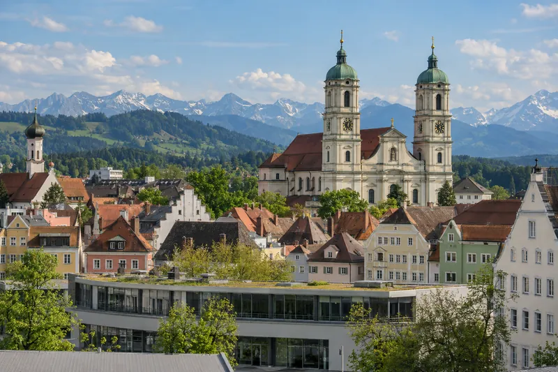 Altstadt von Kempten mit Geschäftshäusern, Basilika im Hintergrund und Allgäuer Voralpen