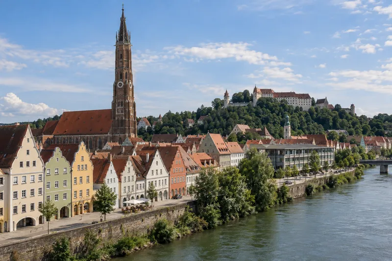 Giebelhäuser in der Landshuter Altstadt mit hohem Backsteinturm und Burg Trausnitz im Hintergrund