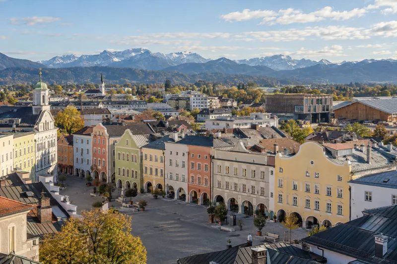 Geschäftshäuser im Inn-Salzach-Stil in Rosenheim, dahinter Gewerbebauten und die Alpen