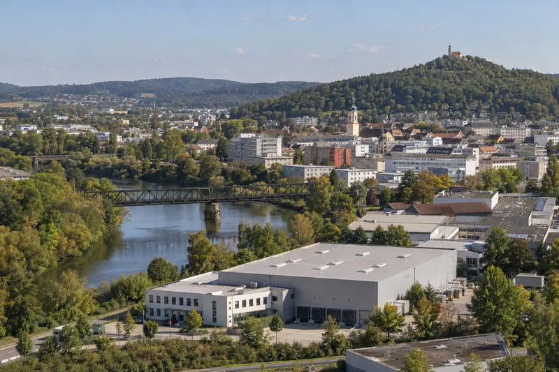 Gewerbehalle mit Bürotrakt in Schwandorf, dahinter die Naab mit Bahnbrücke und der bewaldete Kreuzberg